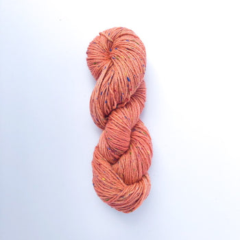 A skein of Donegal Tweed DK yarn in orange color with a tweedy texture.